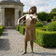 Life-Size Traditional Girl Playing Violin Bronze Sculpture by Giant Sculptures, 180cm, displayed on a gravel garden path beside clipped hedges and a stone pavilion.