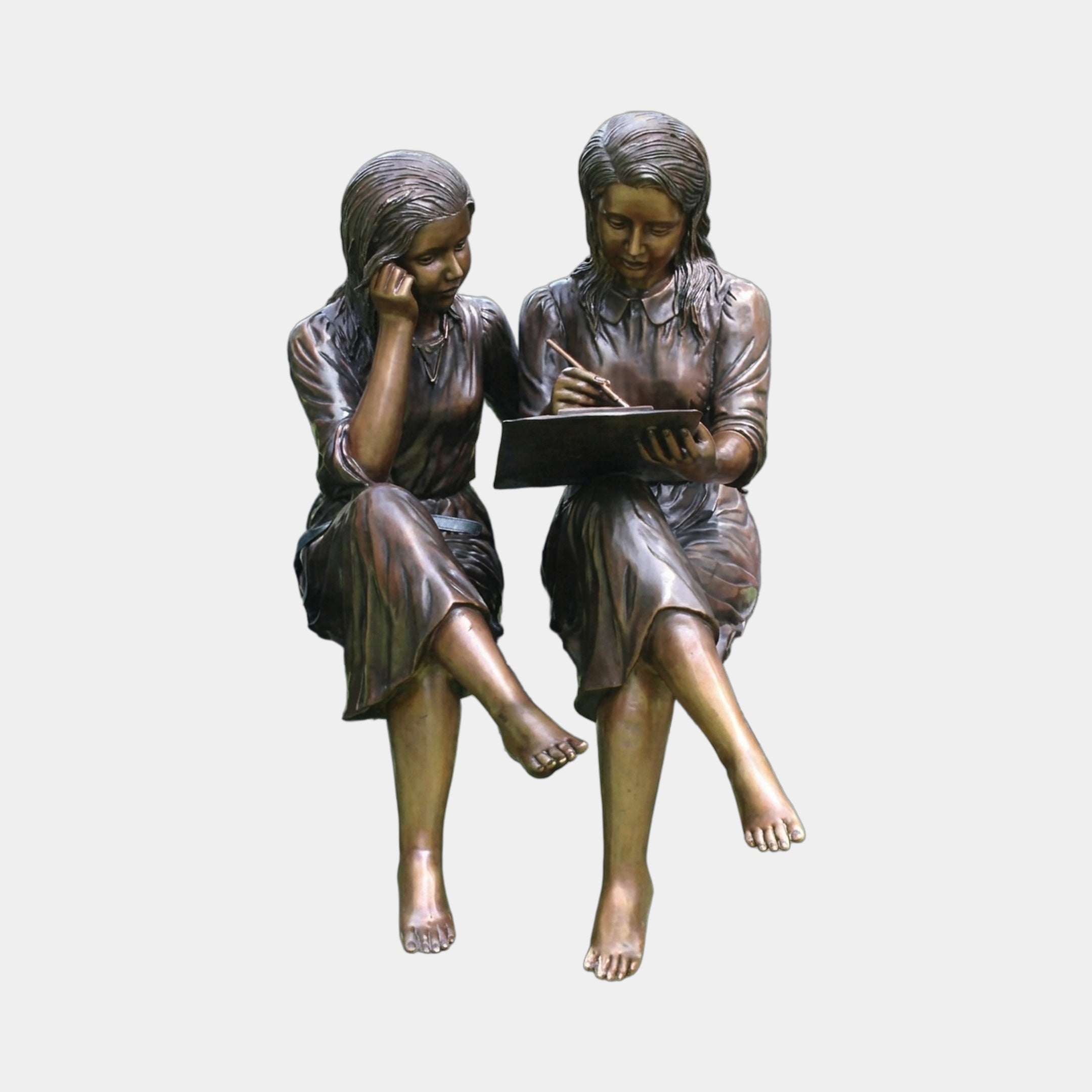 Life-Size Traditional Girls on Bench Bronze Sculpture by Giant Sculptures, showing two barefoot girls seated together as one writes in a book.