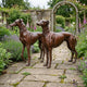 Life-Size Traditional Greyhound and Whippet Pair Bronze Sculpture by Giant Sculptures standing on a stone garden path with lavender and foxgloves.
