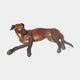 Life-Size Traditional Greyhound Bronze Sculpture by Giant Sculptures, shown reclining with front legs extended and head raised, warm brown patina, on a plain background.