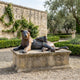 Life-Size Traditional Lioness and Cub Bronze Sculpture by Giant Sculptures on a weathered stone plinth in a walled garden with olive trees and hedges.