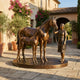 Life-Size Traditional Mare and Foal Bronze Sculpture by Giant Sculptures on a circular plinth in a Mediterranean courtyard with bougainvillea and stone paving.