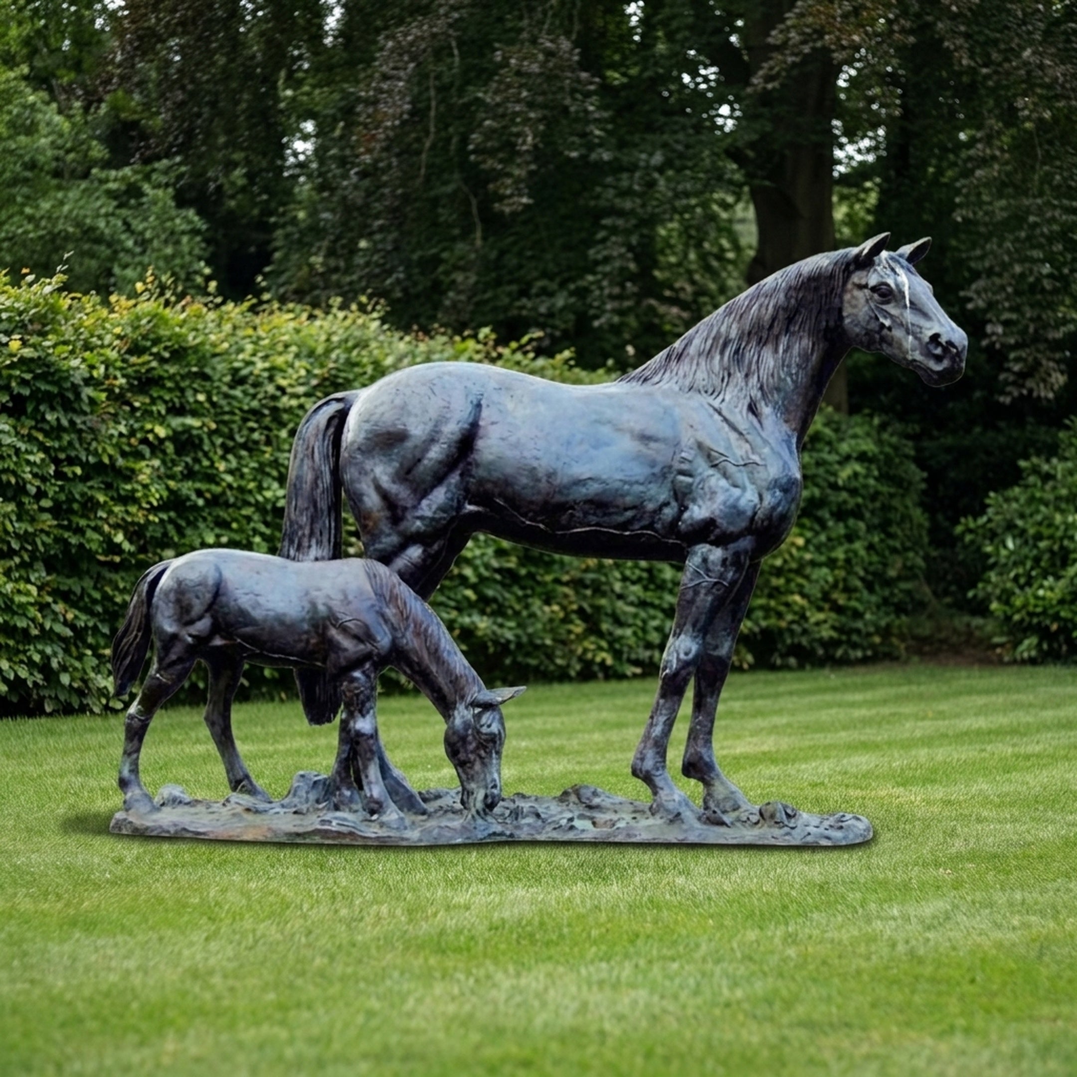 Life-Size Traditional Mare and Foal Bronze Sculpture by Giant Sculptures with blackened patina, mare standing alert beside grazing foal on a lawn before green hedging.