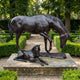 Life-Size Traditional Mare and Foal Bronze Sculpture by Giant Sculptures, dark brown patina, displayed on a stone plinth in a hedged garden pathway.