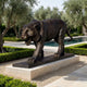 Life-Size Traditional Prowling Tiger Bronze Sculpture by Giant Sculptures, 220cm, snarling mid-stride on a dark plinth in a garden courtyard with olive trees and pool.