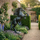 Life-Size Traditional Rearing Horse Bronze Sculpture by Giant Sculptures, dark patina stallion on a rocky base in a walled rose garden with lavender borders.