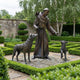 Life-Size Traditional Robed Saint with Wolf and Animal Companions Bronze Sculpture by Giant Sculptures, shown in a formal boxwood garden with stone walls.