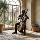 Life-Size Traditional Seated Cellist Bronze Sculpture by Giant Sculptures with dark patina, displayed on stone flooring beside an arched window and potted plants.