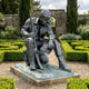 Giant Sculptures Life-Size Traditional Seated Soldier Bronze Sculpture with head bowed, holding a rifle and helmet, on a granite plinth in a hedged garden.