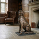 Life-Size Traditional Sitting Labrador Bronze Sculpture by Giant Sculptures displayed on a black base in a wood-panelled library beside a leather wingback chair.