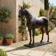 Life-Size Traditional Standing Horse Bronze Sculpture by Giant Sculptures with dark brown patina on a rectangular base, displayed in a gravel Mediterranean courtyard.