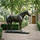 Life-Size Traditional Standing Horse Bronze Sculpture by Giant Sculptures with head lowered and turned, displayed on a black base along a gravel garden path.