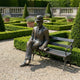 Life-Size Traditional Suited Man on Bench Bronze Sculpture by Giant Sculptures, seated figure in bowler hat with book, set on gravel in a formal garden.