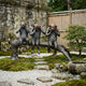 Life-Size Traditional Three Wise Monkeys Bronze Sculpture by Giant Sculptures, dark patina figures on a log in a Japanese moss garden with bamboo fence and maple.