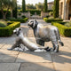 Life-Size Traditional Tiger Pair Bronze Sculpture by Giant Sculptures, one reclining and one standing, displayed on a stone-paved garden path with cypress trees.