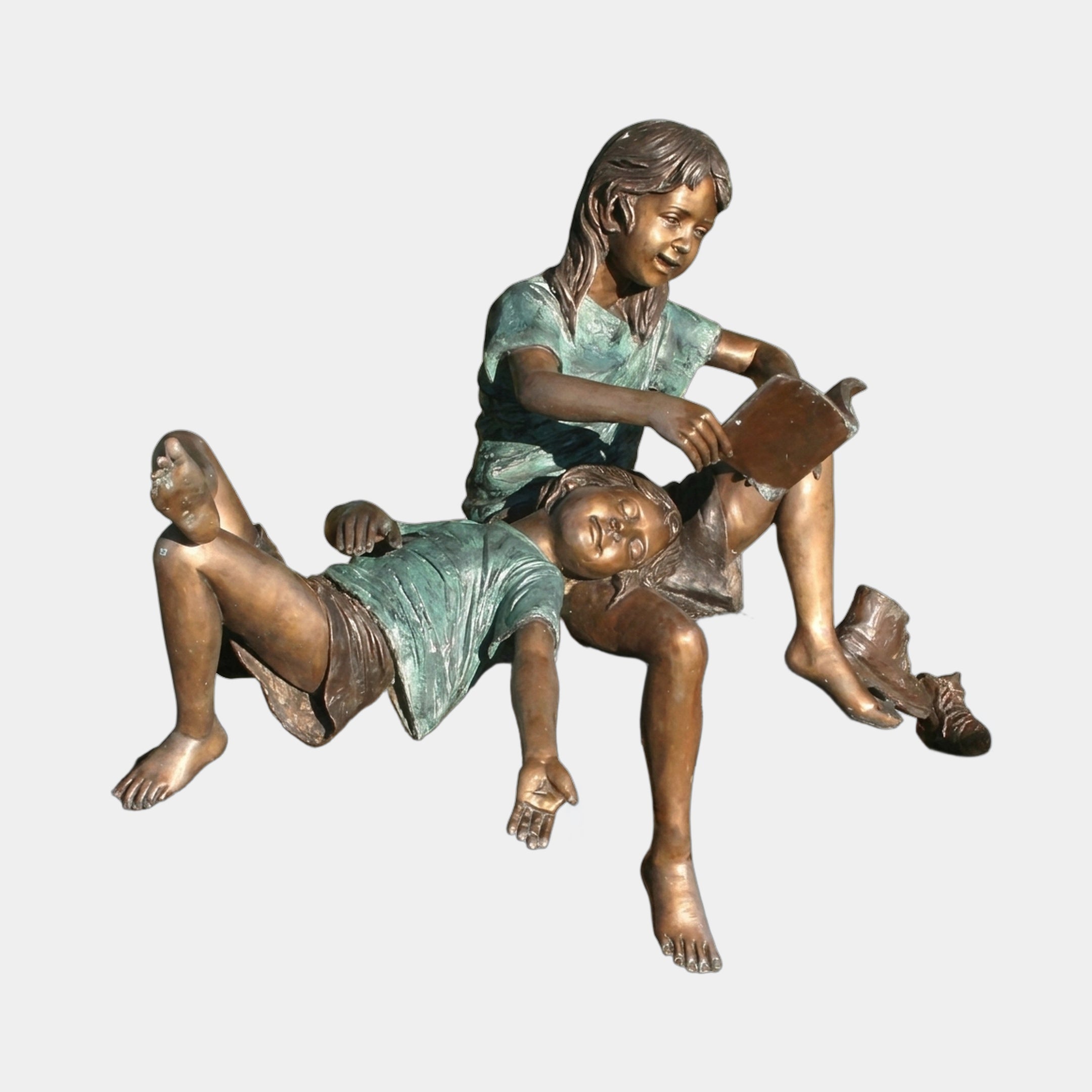 Life-Size Traditional Two Children Bronze Sculpture by Giant Sculptures, showing a seated girl reading to a younger child reclined across her lap, in warm brown and verdigris patina.