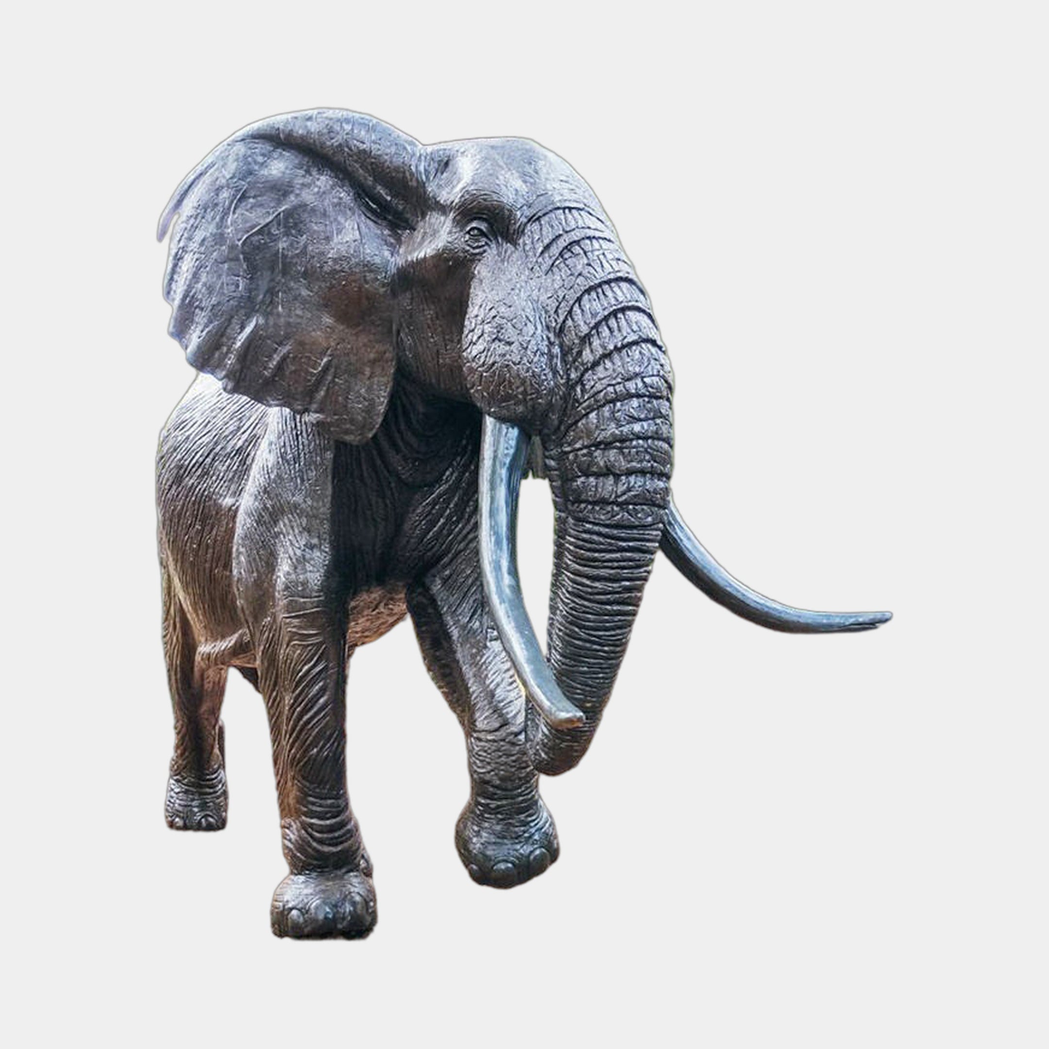 Life-Size Walking African Elephant Bronze Sculpture by Giant Sculptures, shown mid-stride with trunk lowered, long tusks, and dark patina against a plain background.