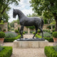 Life-Size Walking Horse Bronze Sculpture by Giant Sculptures in dark patina, foreleg raised on a rocky base atop a stone plinth in a lavender garden.