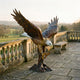 Monumental Bald Eagle Landing Bronze Sculpture by Giant Sculptures, wings raised and talons spread on a branch base, displayed on a stone balustraded terrace.
