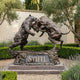 Monumental Bull and Bear Bronze Sculpture by Giant Sculptures, rearing bear and lunging bull locked head-to-head on a granite plinth engraved "Stifel" in a garden.