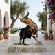 Monumental Charging Bull Bronze Sculpture by Giant Sculptures on a stone plinth in a Mediterranean poolside courtyard with olive trees and bougainvillea.