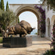 Monumental Charging Bull Bronze Sculpture 320cm by Giant Sculptures on a dark granite plinth in a Mediterranean courtyard framed by an archway over the sea.