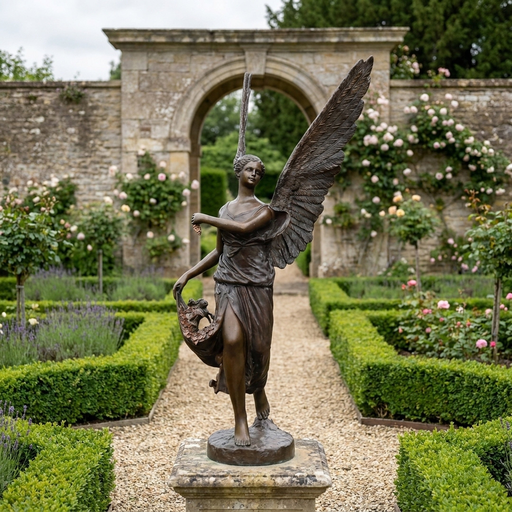 Monumental Classical Angel with Flower Basket Bronze Sculpture by Giant Sculptures, 240cm, displayed on a stone plinth in a formal rose and lavender garden.