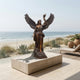 Monumental Classical Angel with Torch Bronze Sculpture by Giant Sculptures displayed on a travertine plinth on a beachfront terrace overlooking the ocean.