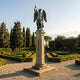 Monumental Classical Archangel Michael Bronze Sculpture by Giant Sculptures, verdigris winged warrior raising a sword atop a cream stone column in a formal hedge garden.