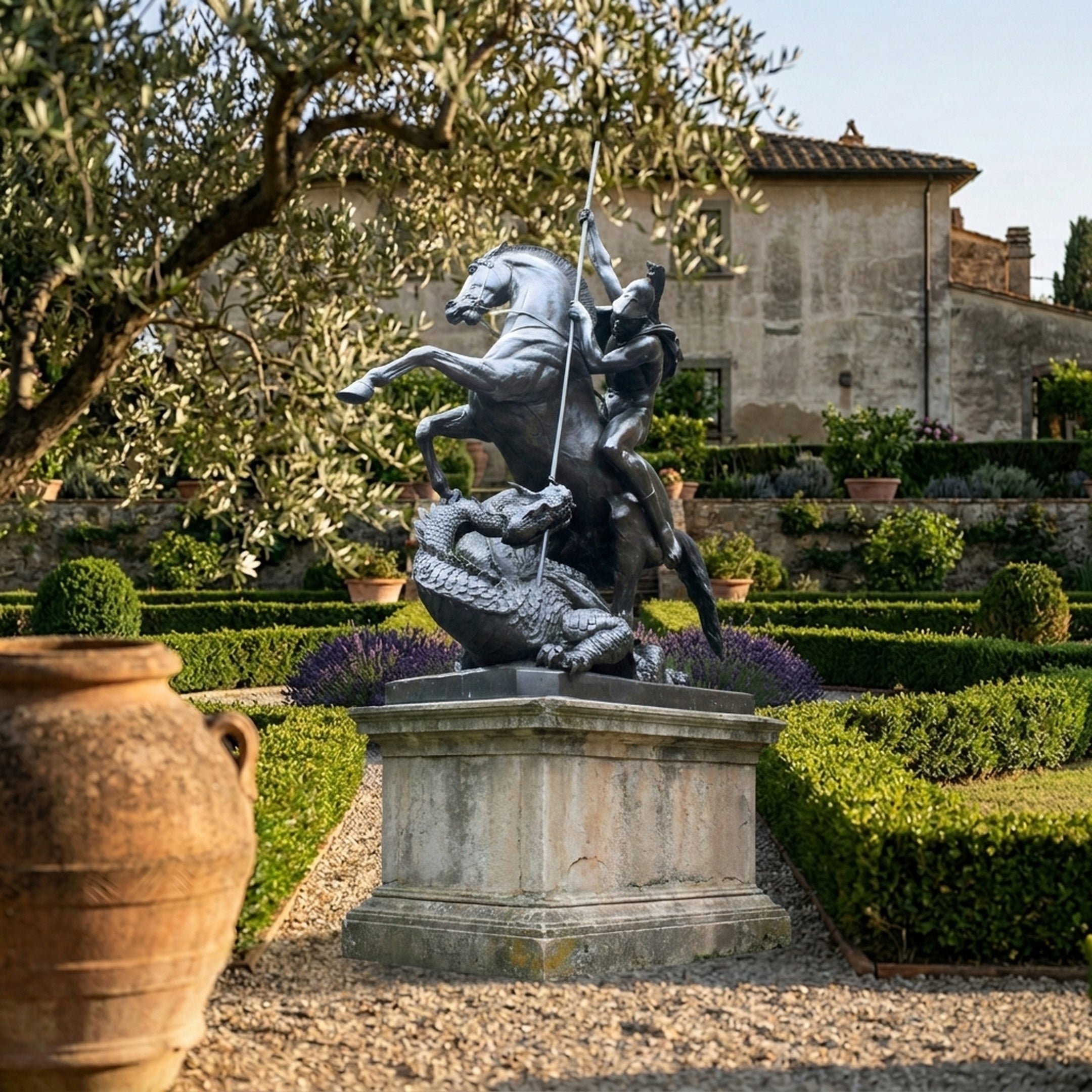 Saint George and the Dragon Bronze Statue by Giant Sculptures on a stone plinth in a Tuscan formal garden with clipped hedges and an olive tree.