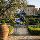 Saint George and the Dragon Bronze Statue by Giant Sculptures on a stone plinth in a Tuscan formal garden with clipped hedges and an olive tree.