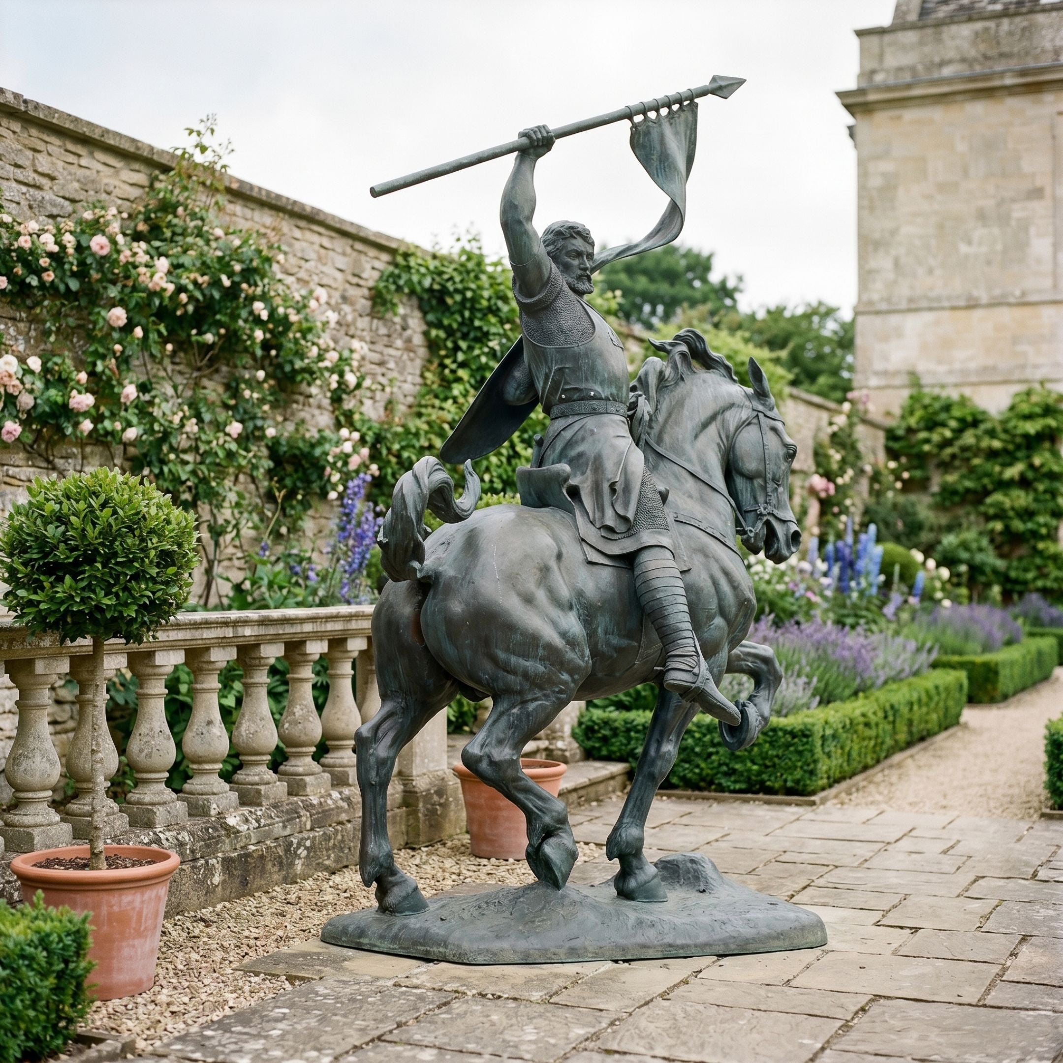 Monumental Classical Armoured Warrior on Rearing Horse Bronze Sculpture by Giant Sculptures, dark antique patina, displayed on a stone garden path beside roses.