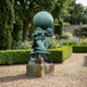 Verdigris bronze Monumental Classical Atlas Kneeling with Globe and Lion sculpture by Giant Sculptures on a stone plinth in a hedged formal garden.