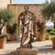 Monumental Classical Bearded Saint Bronze Statue by Giant Sculptures, 250cm robed figure with raised hand and cross, set on a stone base in an arched courtyard.