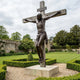 Giant Sculptures Monumental Classical Crucified Christ Bronze Sculpture 500cm with dark patina on a weathered wooden cross, displayed in a walled garden.