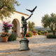 Monumental Classical Falconer and Bird of Prey Bronze Sculpture by Giant Sculptures on a stone pedestal in a Mediterranean courtyard with olive trees.