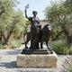 Monumental Classical Female Figure and Lion Bronze Sculpture by Giant Sculptures on a stone plinth in a Mediterranean garden with olive trees and lavender.