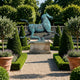 Giant Sculptures Monumental Classical Galloping Horse and Swallow Bronze Sculpture with verdigris patina on a stone plinth in a formal topiary garden.