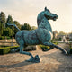Monumental Classical Galloping Horse and Swallow Bronze Sculpture by Giant Sculptures in aged verdigris finish, displayed on a formal garden terrace at dusk.