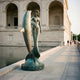 Monumental Classical Mermaid and Dolphin Bronze Sculpture by Giant Sculptures with verdigris patina, displayed beside a reflecting pool along an arched stone building.