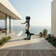 Monumental Classical Mermaid Bronze Statue by Giant Sculptures on a modern oceanfront terrace, her arm raised and tail curling onto a sculpted wave base.