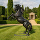 Monumental Classical Rearing Horse Bronze Sculpture by Giant Sculptures, black-brown patina, displayed on a manicured lawn with cypress trees and a stone pavilion.