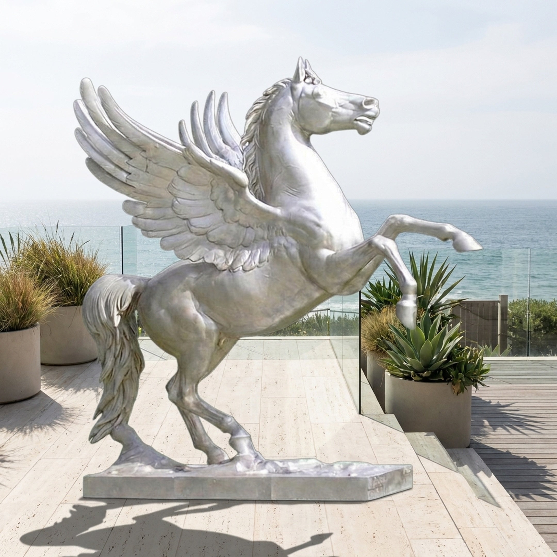Monumental Classical Rearing Pegasus Bronze Sculpture by Giant Sculptures in pale silver finish, rearing on a plinth on a seaside terrace with planters.