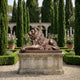 Monumental Classical Recumbent Lion Bronze Sculpture by Giant Sculptures on a stone pedestal in a formal garden with cypress trees and rose bushes.
