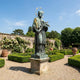 Giant Sculptures Monumental Classical Robed Saint Bronze Sculpture 450cm with verdigris patina, gold star halo and palm frond, on a stone plinth in a walled rose garden.