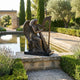 Monumental Classical Seated Angel Harp Bronze Sculpture by Giant Sculptures on a stone plinth beside a reflecting pool with cypress trees and lavender.