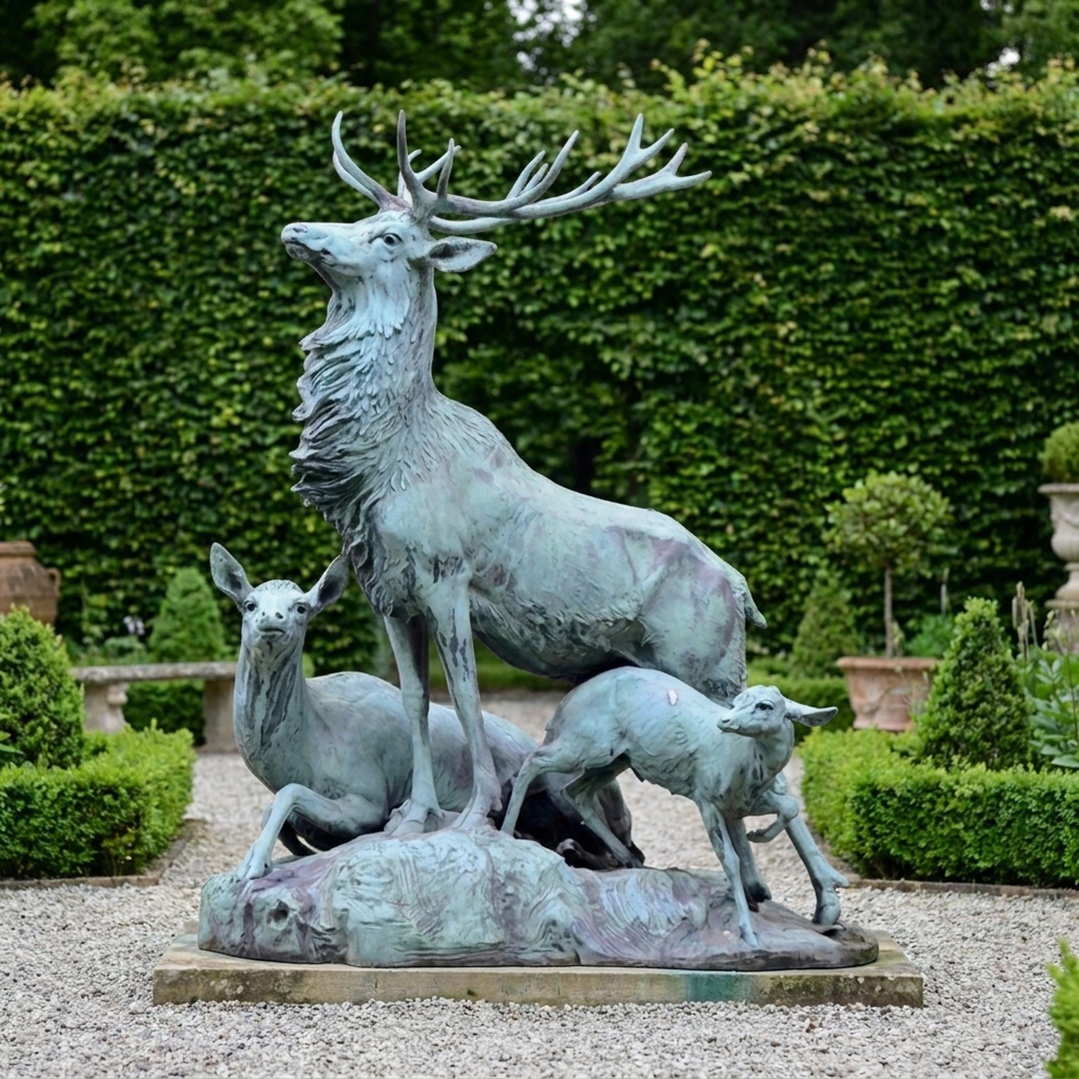 Monumental Classical Stag Doe and Fawn Bronze Sculpture by Giant Sculptures with verdigris patina, displayed on a gravel path before a tall green hedge.