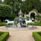 Monumental Classical Three Horses Bronze Fountain by Giant Sculptures with verdigris patina horses mid-stride around a tiered basin in a hedged garden.