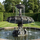 Monumental Classical Tiered Figurative Bronze Fountain by Giant Sculptures, 450cm, with lion-head spouts and cherub base in verdigris patina, set in a garden.