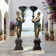 Pair of Monumental Classical Torch-Bearer Goddess Bronze Sculptures by Giant Sculptures, draped figures in gold and verdigris holding lamp standards on a Mediterranean terrace.
